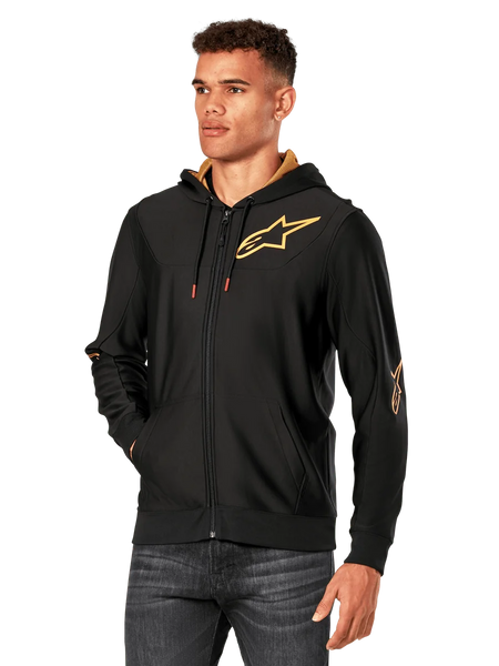 Alpinestars Sessions V3 Hoodie, Black with Gold logos, zip-up fleece hoodie worn by a model with dark jeans, featuring a gold mesh-lined hood and red-tipped drawcords, casual motorsport-inspired streetwear