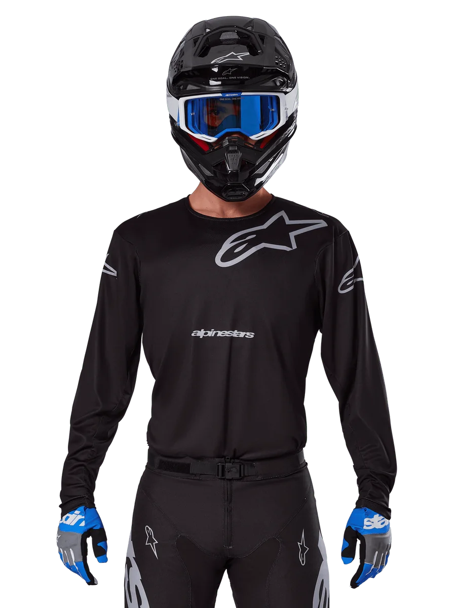 Alpinestars 2025 Racer Graphite Jersey, Motocross Racing Gear, Black with Gray logos, worn with matching black helmet, blue goggles, and blue and gray gloves, form-fitting performance design with chest and arm branding