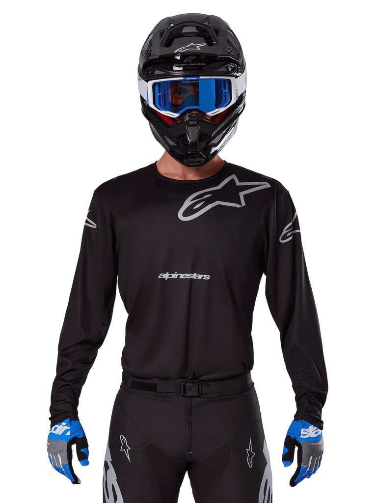 Alpinestars 2025 Racer Graphite Jersey, Motocross Racing Gear, Black with Gray logos, worn with matching black helmet, blue goggles, and blue and gray gloves, form-fitting performance design with chest and arm branding