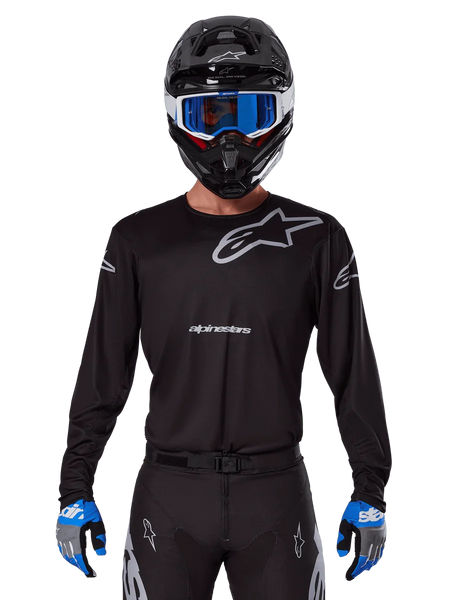 Alpinestars 2025 Racer Graphite Jersey, Motocross Racing Gear, Black with Gray logos, worn with matching black helmet, blue goggles, and blue and gray gloves, form-fitting performance design with chest and arm branding
