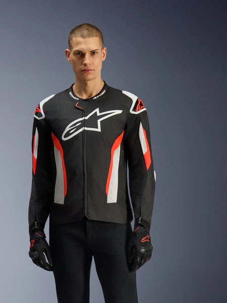 Male model wearing the Alpinestars T-GP Air Jacket, Black with Red Fluo and white accents, large Alpinestars logo on chest, featuring laser-perforated panels and shoulder armor, worn with black riding gloves, sport-cut motorcycle gear for warm weather