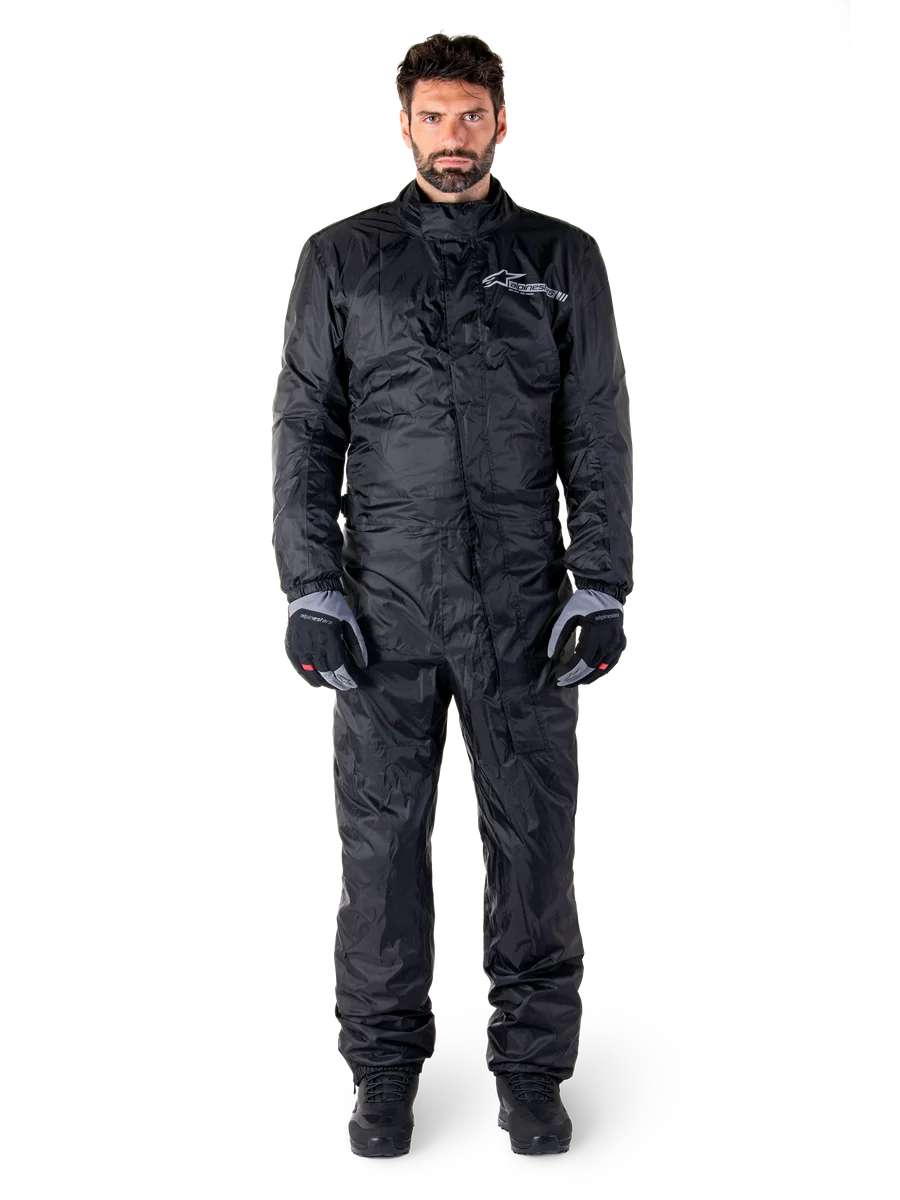 Alpinestars Hurricane Rain V2 Suit, Full-Body Motorcycle Rain Suit in Black, waterproof protective gear with high collar and front storm closure, featuring white logo on chest, worn with black and grey gloves and boots