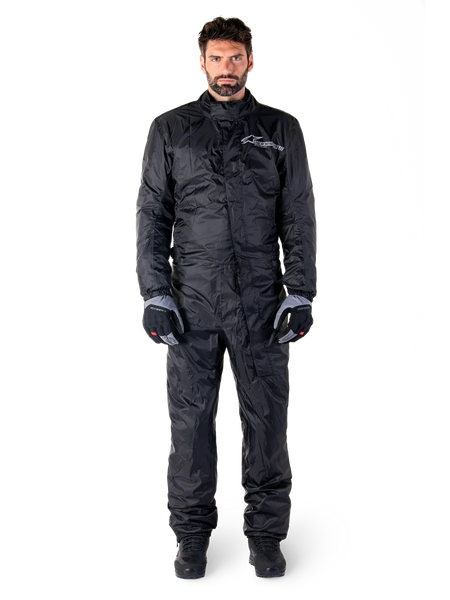 Alpinestars Hurricane Rain V2 Suit, Full-Body Motorcycle Rain Suit in Black, waterproof protective gear with high collar and front storm closure, featuring white logo on chest, worn with black and grey gloves and boots