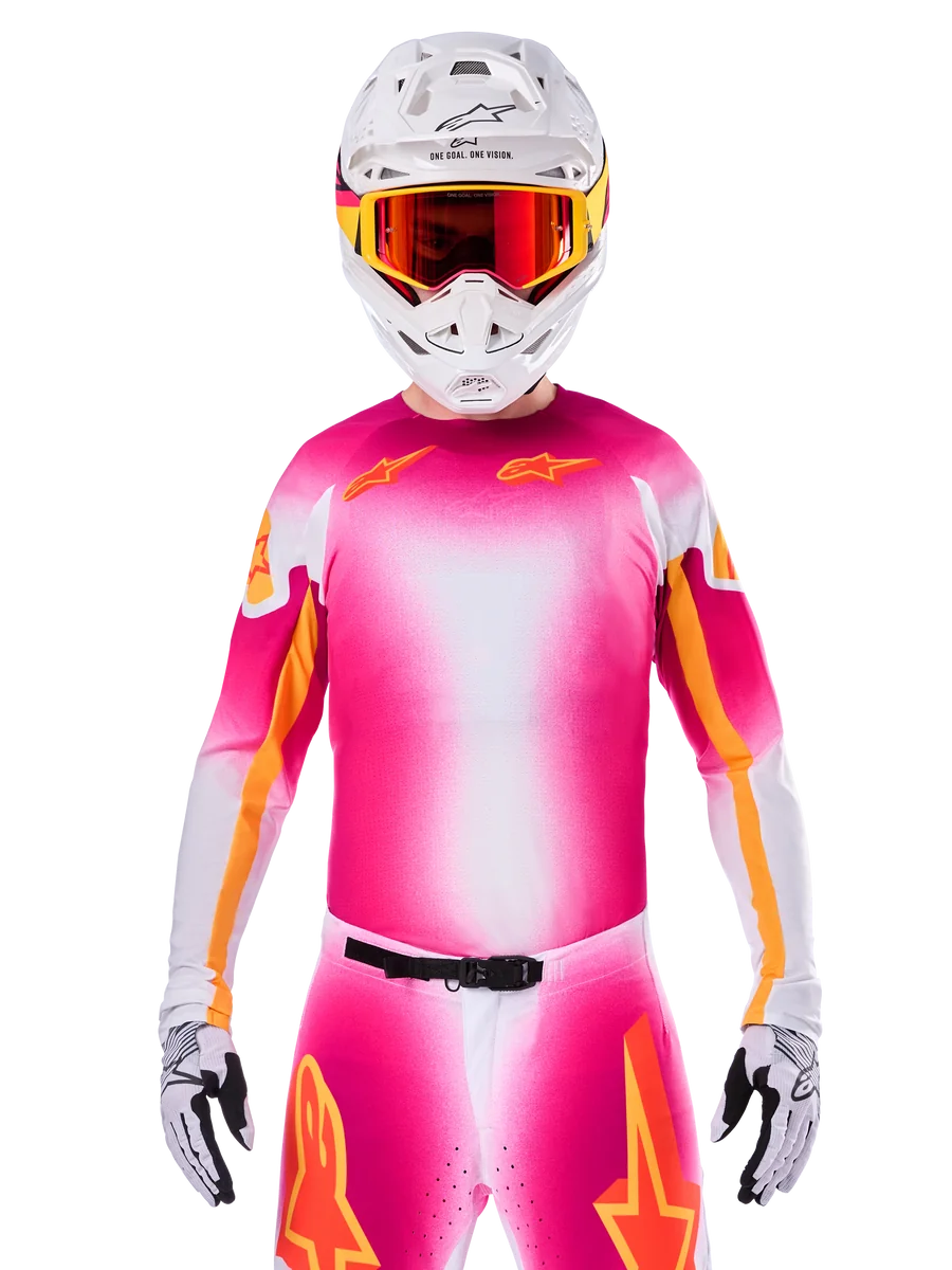 Motocross rider wearing the Alpinestars Limited Edition Supertech AFD MIG Jersey, Pink Fluo White gradient design with orange star logos, matching pants, white helmet, and red-tinted goggles, elite off-road racing apparel.