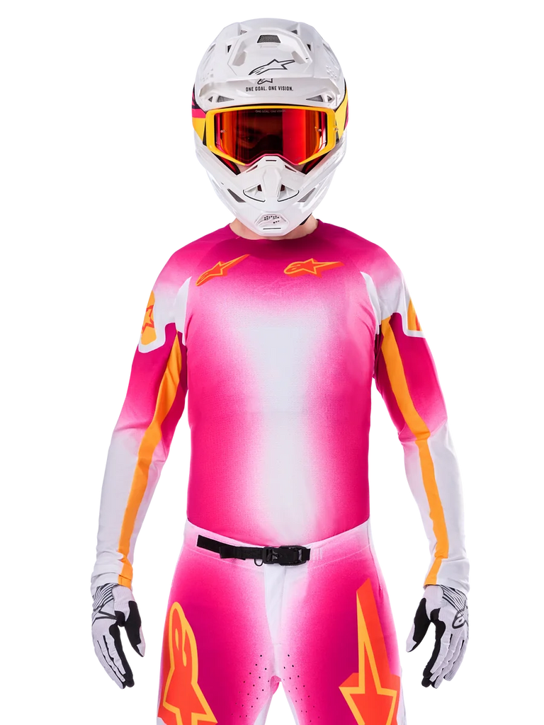 Motocross rider wearing the Alpinestars Limited Edition Supertech AFD MIG Jersey, Pink Fluo White gradient design with orange star logos, matching pants, white helmet, and red-tinted goggles, elite off-road racing apparel.